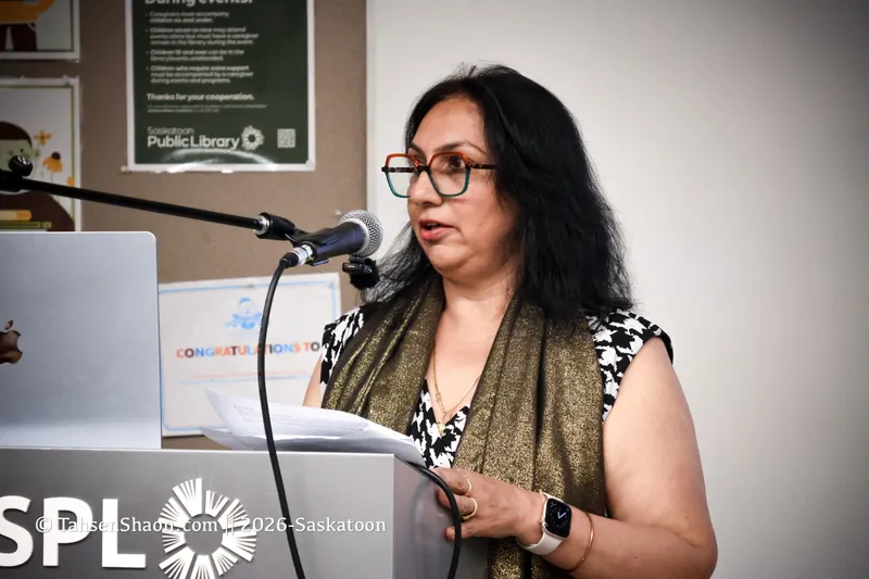A speaker in glasses at the podium, with notes in hand